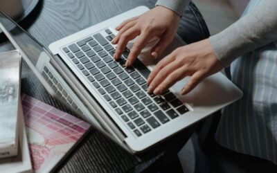 Deux mains tapent sur le clavier d'un ordinateur portable blanc, assis à un bureau