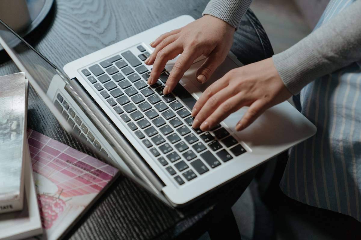 Deux mains tapent sur le clavier d'un ordinateur portable blanc, assis à un bureau