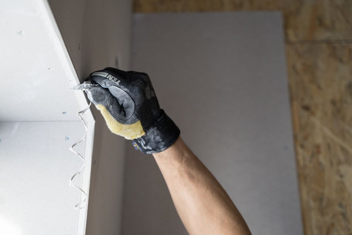 Une main gantée applique de la pâte à joint sur un mur blanc