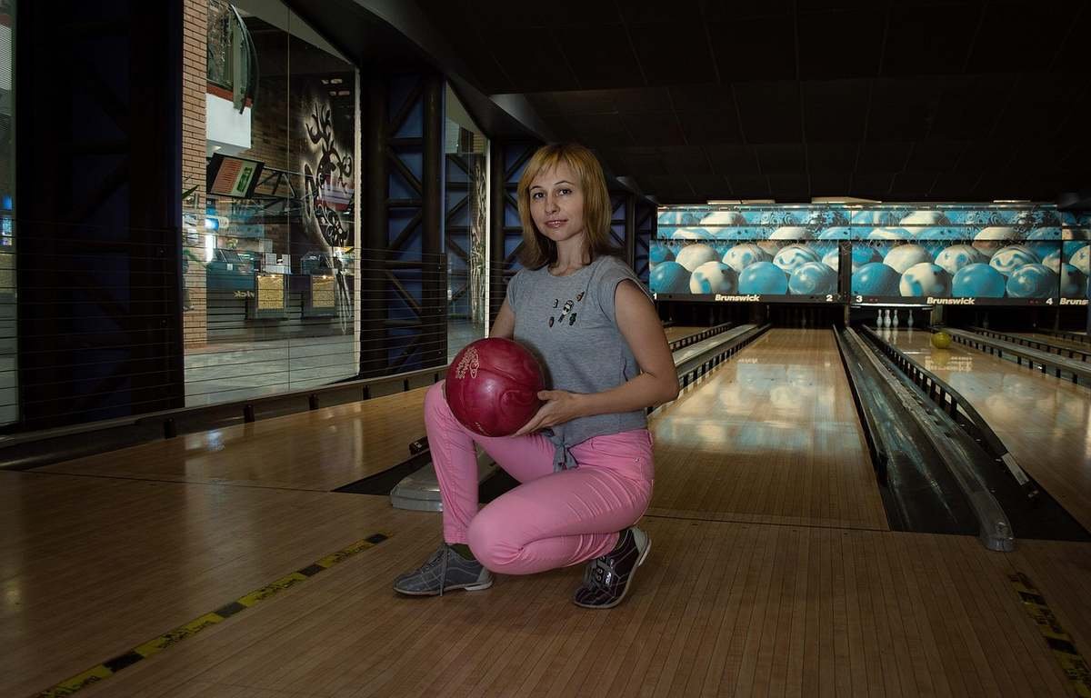 Une femme en tenue rose s'agenouille avec une boule de bowling